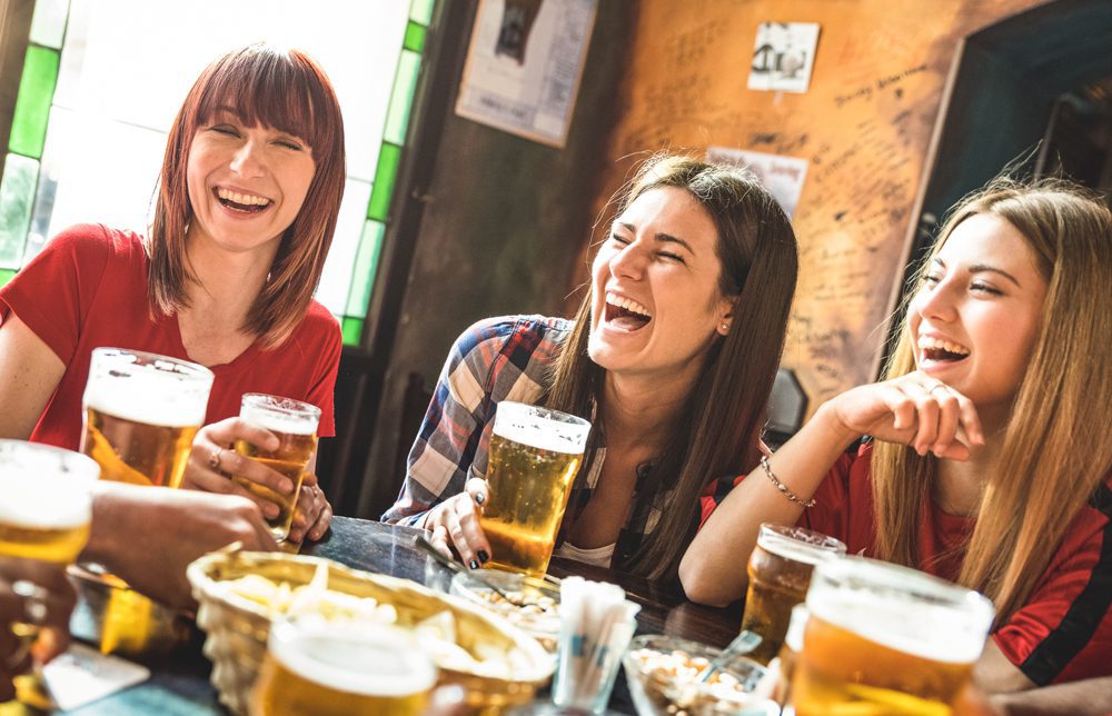 Happy girlfriends women group drinking beer at brewery bar restaurant - Friendship concept with young female friends enjoying time and having genuine fun at cool vintage pub - Focus on left girl Three women laugh at a restaurant table with glasses of beer