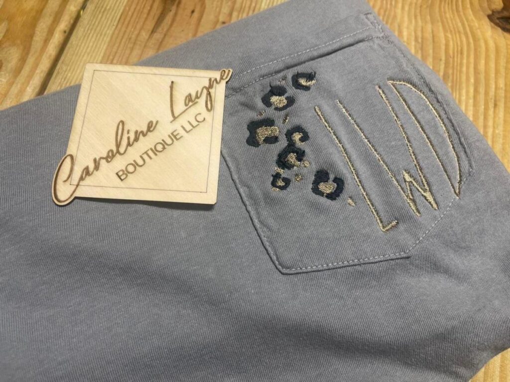 A gray knit piece of clothing with leopard print embroidery and a tag reading Caroline Layne Boutique LLC