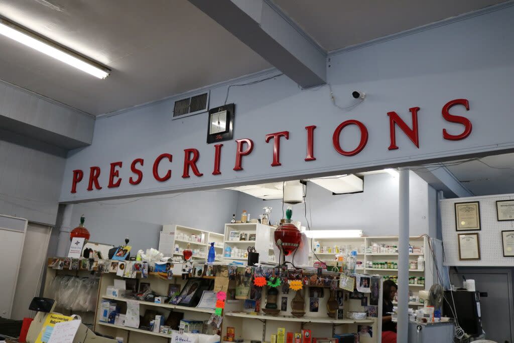 A pharmacy counter inside a store with a large red sign above the counter reading Prescriptions