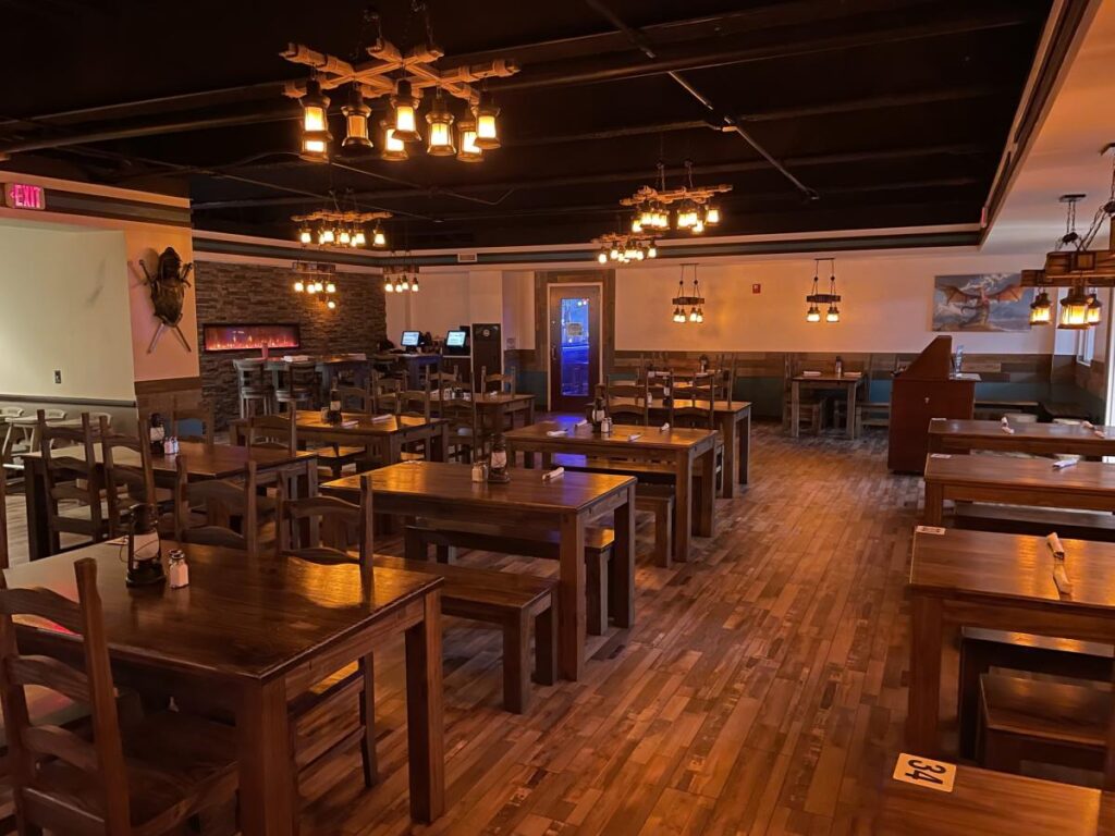 The interior of a tavern with empty brown wooden tables and chairs and a wooden floor
