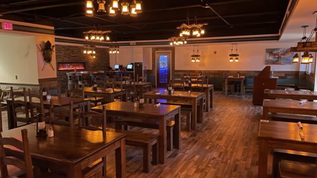 The interior of a tavern with empty brown wooden tables and chairs and a wooden floor