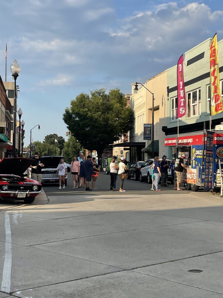 People wait in line at a food truck parked on a street.