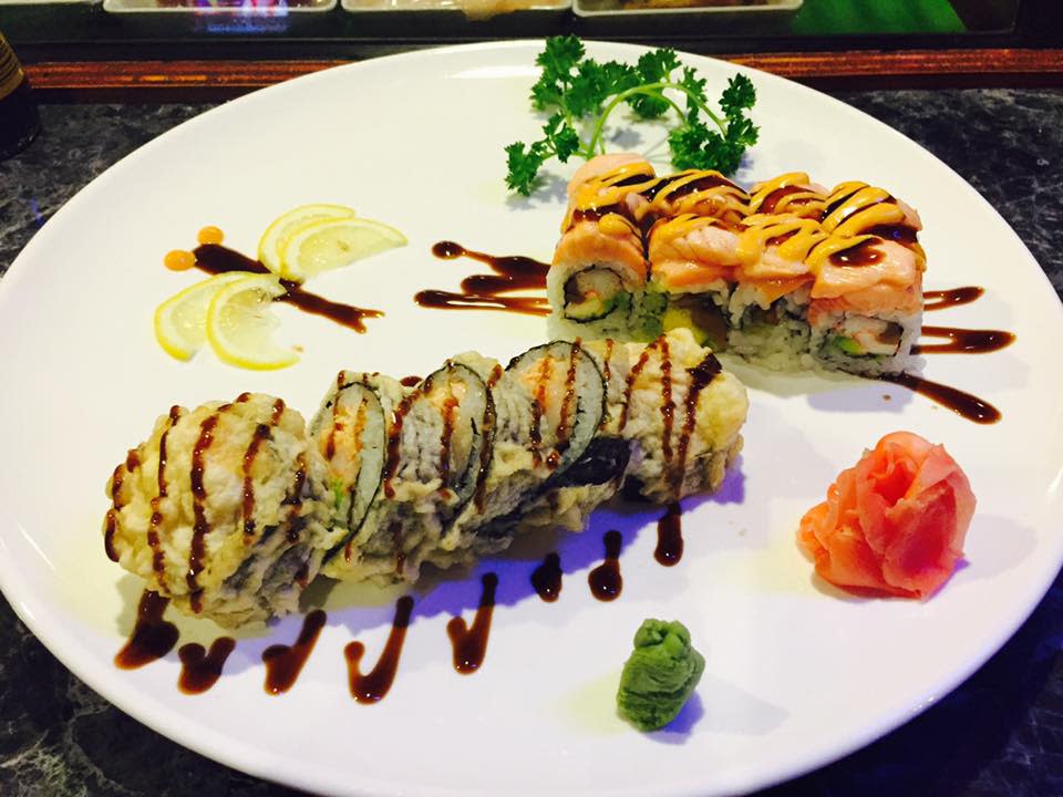 Two sushi rolls, wasabi and ginger displayed on an oval white plate
