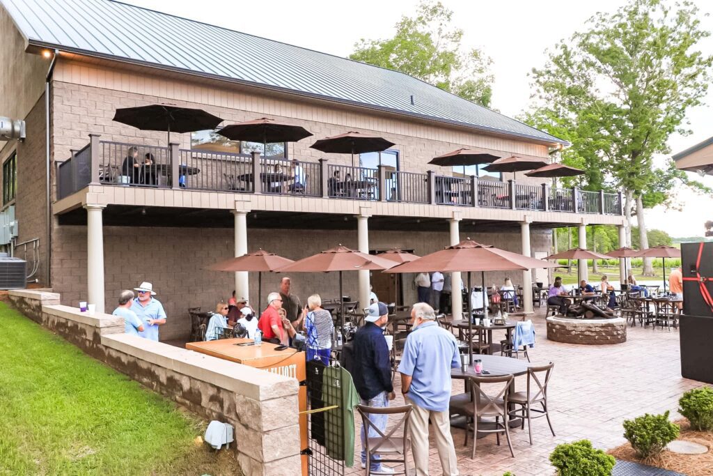 Small groups of people chat in an outdoor courtyard surround by small tables and brown umbrellas