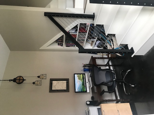 A small wooden desk with a computer next to a white staircase