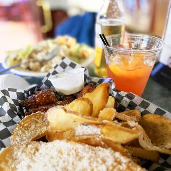 Chicken wings and fries served in a basket with black and white checked paper