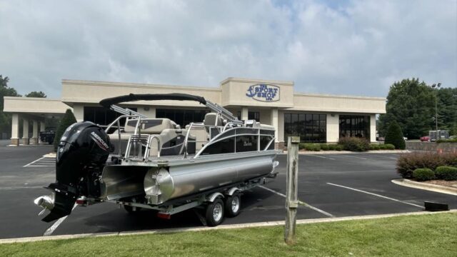 A motorboat sits on wheels in a parking lot outside a sport shop