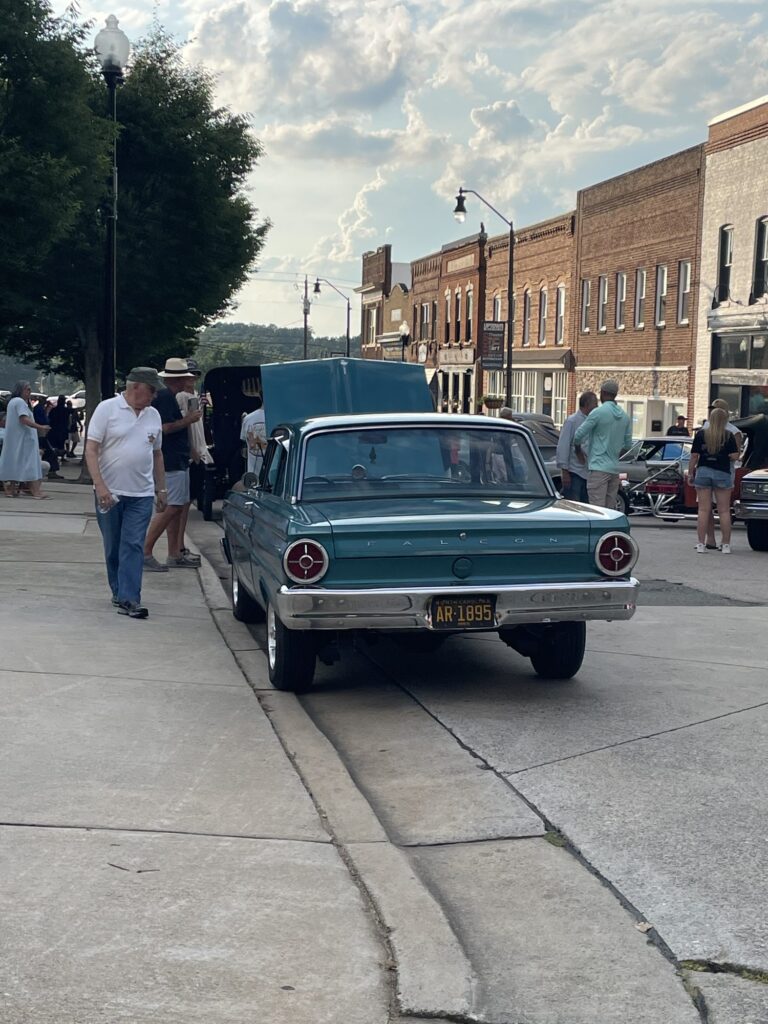 People look at a blue classic car with a raised hood.
