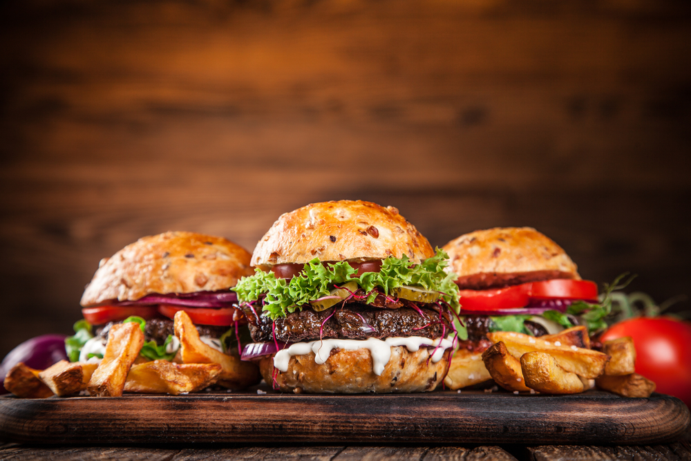 Three cheeseburgers sit on a wooden platter surrounded by French fries