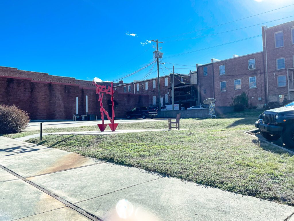 A red metal art sculpture on a concrete pad with a bench nearby